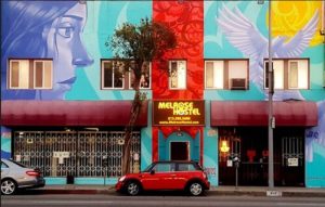 Melrose Hostel Adults Only: Gay-friendly hotel facade with colorful murals, red Mini Cooper parked in front. Great for gay travel in LA.