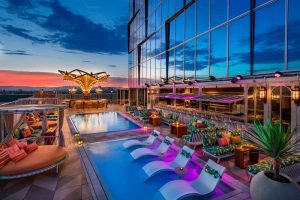Rooftop pool at Moxy Downtown Los Angeles, a gay-friendly hotel. Lounge chairs, bar, and city views at dusk. Perfect for LGBTQ+ travelers.