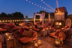 Petit Ermitage Hotel adults-only rooftop terrace at dusk. Cozy seating, fireplace, and string lights create a romantic, gay-friendly ambiance.