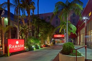 Ramada Plaza by Wyndham West Hollywood Hotel & Suites entrance. Gay-friendly hotel with palm trees and illuminated signage at night.