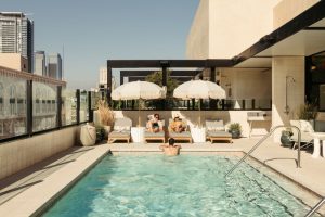 Rooftop pool at The Hoxton Downtown LA, a gay-friendly hotel. People relax on loungers under umbrellas. Great spot for gay travelers.