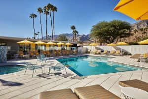 Twin Palms Resort, Palm Springs' gay men's getaway. Poolside loungers, yellow umbrellas, palm trees, and mountain views create a relaxing vibe.