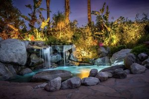 Vista Grande Resort, a gay men's resort. Waterfall feature with rocks and tropical plants, illuminated at night. Gay-friendly hotel.
