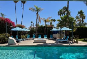 Desert Paradise Resort Hotel pool area, Palm Springs. Turquoise lounge chairs, umbrellas, and a fire pit create a relaxing gay hotel vibe.