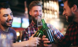 Three gay men toasting beers at a Long Beach gay bar. Friends enjoying drinks at one of the best gay bars updated this year.
