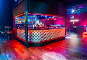 Interior of Club Cobra bar. Bottles line shelves behind the bar. Red curtains and a disco ball add to the gay bar's atmosphere.