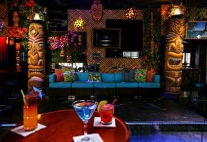 Toucans Tiki Lounge interior. Gay bar with tiki statues, bamboo wall, blue sofa, and tropical cocktails. Gay travel destination.
