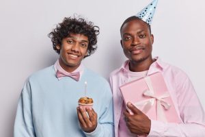 Gay couple celebrating anniversary in NYC. Man with cupcake and candle, other with gift and party hat. Perfect anniversary.