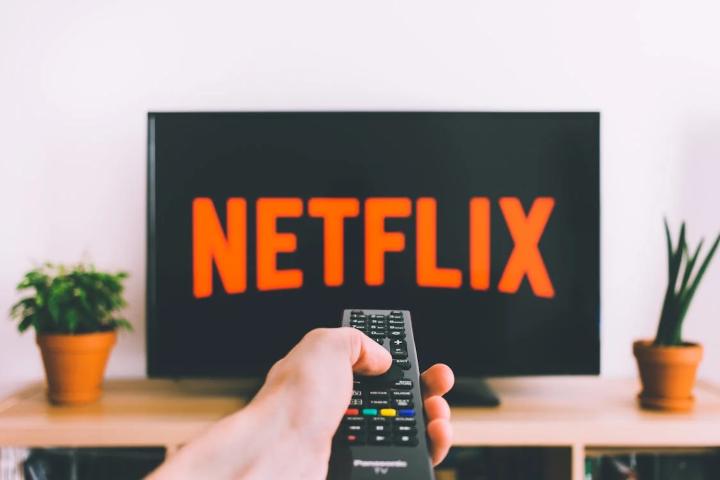 Netflix abroad. Hand holding remote, Netflix logo on TV. Georestrictions travelers may face when abroad. Gay travel advice.