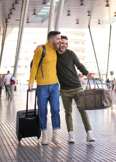Gay couple excited for cheap flights to amazing destinations. Men with luggage ready for last-minute travel.