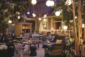 Gay-Friendly NoMad Las Vegas hotel outdoor patio. Tables and chairs under trees with globe lights. A perfect spot for gay travelers.