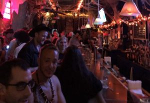 Interior of 9th Avenue Saloon, a gay bar in New York City, decorated for Halloween. Patrons are standing at the bar, enjoying drinks.