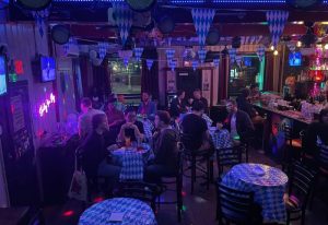 Inside Albatross Bar, New York. Gay bar scene with patrons at tables, bar with Pride sign, blue & white decor. Gay travel advice.