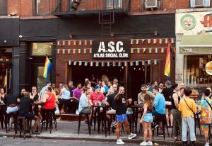 Atlas Social Club in New York. Gay bar scene with rainbow flags. People socializing at the outdoor tables. Gay travel destination.
