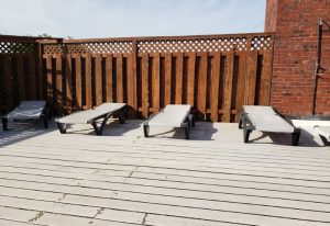 Bain Colonial Bath, a gay spa in Montreal: Lounge chairs on a wooden deck with a fence and brick wall. Perfect for relaxation.