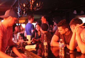 Barracuda Lounge, a gay bar in New York. People at the bar, drinking and socializing. Nightlife scene, bar tender, and antler chandelier.