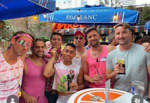 Toronto Gay Bars: Group of gay men at an outdoor patio bar. Rainbow flags visible. Best Toronto Gay Bars for gay travel advice.