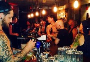 Inside Black Eagle cruising bar, Toronto. Tattooed bartender pours a beer. Gay bar scene with men in leather and casual wear.