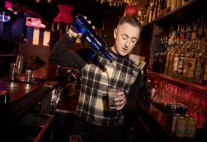 Alan Cumming pours a drink at his gay bar Club Cumming in New York. Gay travel advice.