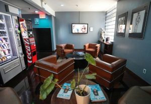 East Side Club, New York gay sauna lounge area. Brown leather chairs, vending machines, TV, and artwork. Relaxing space for gay men's travel.