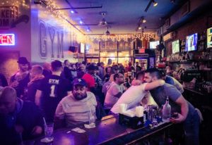 Busy GYM Sportsbar in NYC. Gay bar scene with men socializing at the bar. Nightlife in New York City. Travel advice.