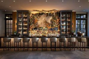 Interior of 1 Hotel Toronto's bar. This gay-friendly hotel bar features a floral backdrop, stools, and liquor cabinets. Upscale and modern.