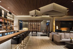 Interior of gay-friendly JW Marriott Parq Vancouver hotel. Bar with stools, lounge seating, decorative ceiling, and display case. Upscale design.