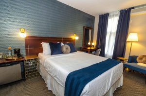 Maison Cartier Montreal gay-friendly hotel room. A bed with blue accents, desk, and sitting area. Upscale lodging for gay travelers.
