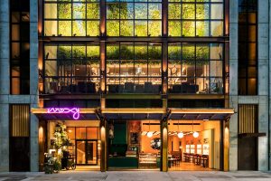 Moxy NYC Chelsea hotel exterior. Gay-friendly hotel with a neon sign, greenery, and a bar. A top choice for gay men visiting NYC.