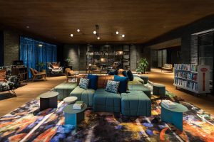 Moxy NYC East Village hotel's stylish lounge. Modern design, colorful rug, modular seating, and bookshelves create a welcoming, gay-friendly space.