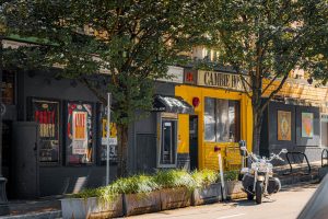 Cambie Hostel Gastown's exterior. This gay-friendly hotel features a motorcycle parked outside. A vibrant yellow facade stands out.