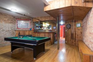 Wrigley Hostel Adults Only game room. Pool table, dartboard, and bar area in a gay-friendly hotel. Wood paneling and exposed brick details.