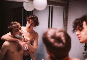 Gay-friendly hotel in Montreal: Two shirtless men in a bathroom. One is shaving the other's face with shaving cream and a razor.