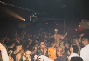 HUSH HK gay bar, dance club in New York. Crowd of gay men dancing, shirtless dancer on stage. Nightlife, travel advice, gay scene.