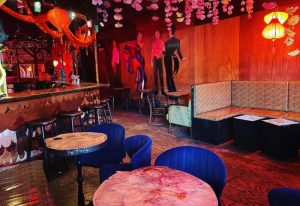Interior of Happyfun Hideaway, a gay bar in New York. Decorated with colorful lanterns, murals, and cozy seating areas. Gay travel advice.