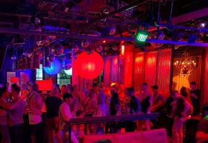 Industry Bar in New York: A vibrant gay bar with a crowd of men enjoying the nightlife. Disco balls & colorful lights create a lively atmosphere.
