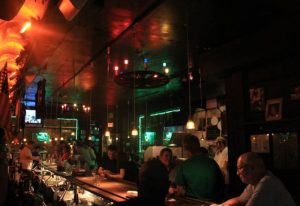 Interior of Julius' Gay Bar in New York. Patrons at the bar, with warm lighting and American flags. Gay travel advice.