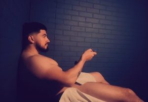 Man relaxing in a sauna, part of Las Vegas gay cruise clubs. He's holding a remote, enjoying the spa experience. Gay travel advice.