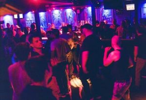 Montreal gay bar scene: Le Stud bar interior, crowded with gay men. Red and blue lighting, artwork on the walls. Gay travel advice.