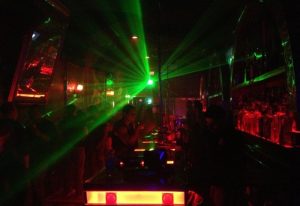 Les Hommes Gay Bar: Interior view of a crowded gay bar in New York with green laser lights and red bar lighting. Nightlife scene.