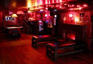 Nowhere Bar in New York City. Red lighting, pool table, benches, fireplace, arcade games. Gay bar travel advice, nightlife.