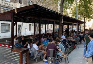 Outdoor seating at Pieces Bar in New York. People sit at tables under a covered patio. A popular gay bar in NYC. Gay travel.