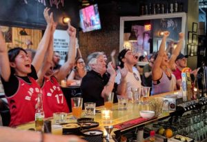 Excited fans at Score on Davie sports bar in Vancouver. People cheering, watching a game, enjoying drinks. Gay-friendly sports bar atmosphere.