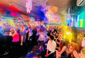 Suite Bar, NYC gay pub, Halloween party. People enjoy the festive atmosphere, with colorful lights and decorations. Gay travel in New York.