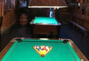 Interior of The Cinch Saloon, a gay bar in San Francisco. Pool tables, bar stools, and a barrel are visible, creating a classic saloon vibe.