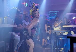 Drag queen performs at The Drink, a gay pizza bar in Toronto. Patrons watch the show in the bar's smoky, atmospheric interior.