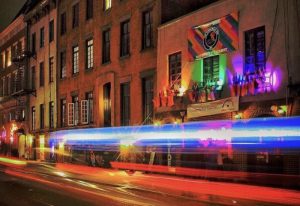 Night view of The Stonewall Inn in New York. Historic gay bar with rainbow flag, lights, and traffic streaks. Gay travel destination.