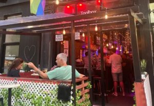 The ToolBox Bar in New York, a gay bar with an outdoor seating area. People are drinking and socializing. Rainbow flag visible. Gay travel advice.