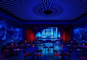 The Times Square EDITION's Paradise Club. A design hotel in Hell's Kitchen gayborhood. Blue lights, stage, tables, chairs, red curtains.