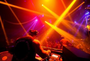 DJ at a Puerto Vallarta gay bar, DSC07645. Muscular DJ with headphones, crowd, and bright lights. Gay nightlife in Puerto Vallarta.